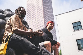 Photo of Two  Men in  Long-sleeved Shirts Sitting on a Statue Near a Building