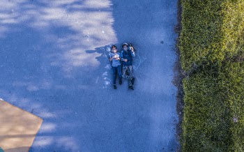 Photo of Two Person Lying on Road Near Green Grass Field