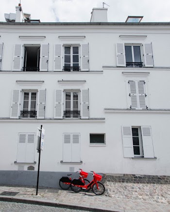 Photo of Two Red Bicycles Parked on the Sidewalk Next to a White Building