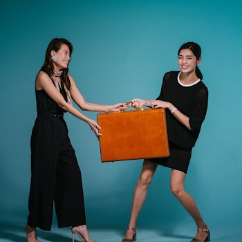 Photo of Two Smiling Women Fighting Over Suitcase