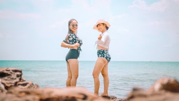 Photo of Two Smiling Women Standing on Rocks Near Body of Water
