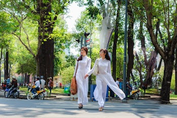 Photo of Two Women In White Outfits Holding Hands While Crossing the Street