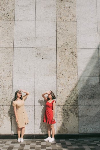 Photo of Two Women Standing by Wall Posing While  Blocking Sun with Their Hands