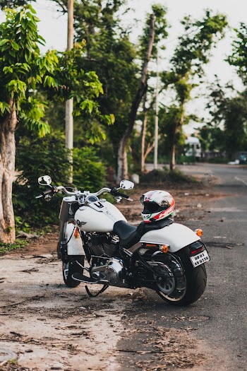 Photo of White Harley Davidson Fatboy Cruiser Motorcycle  with Helmet on Seat Parked by Side of Road Next to Trees