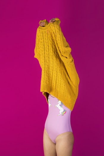 Photo of Woman About to Wear Off Yellow Sweater in Pink Background