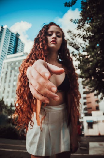 Photo of Woman Black Brassiere and White Miniskirt Leaning Forward While Posing With Her Hand Out