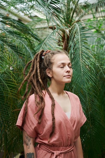 Photo of Woman Closing Her Eyes While Standing Near Green Leaves