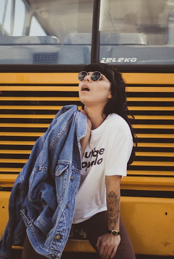 Photo of Woman Holding Blue Denim Jacket While Sitting on Yellow Bus Bumper