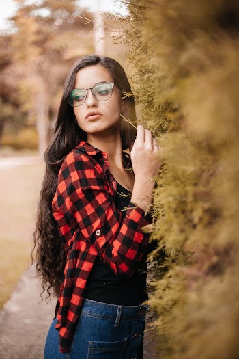 Photo of Woman in a Red and Black Checkered Shirt Standing Beside Hedge