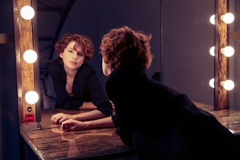 Photo of Woman in Black Coat Posing In Front of Vanity Mirror
