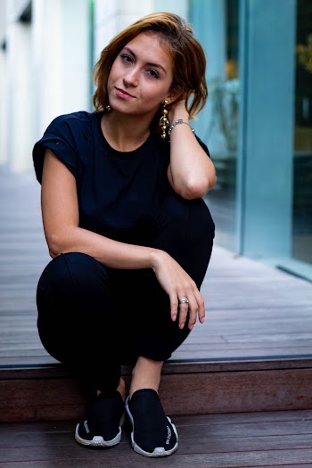 Photo of woman in black crew-neck t-shirt and black pants sitting down with her hand behind her head