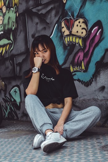 Photo of Woman in Black Crew-neck T-shirt and Gray Track Pants Sitting Beside Graffiti Wall