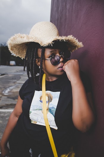 Photo of Woman in Black Graphic T-shirt and Brown Hat Posing Against Maroon Painted Wall While Clenching Fist