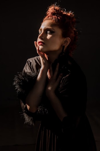Photo of Woman in Black Long-sleeved Dress Posing With Her Eyes Closed In Front of Black Background