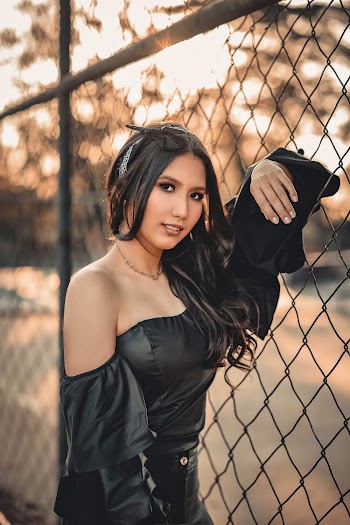 Photo of Woman in Black Outfit Leaning on Chain-link Fence Posing