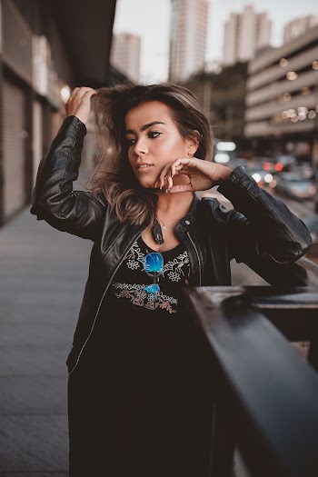 Photo of Woman in Black Outfit Standing on Side Walk by Metal Railing Posing While Looking Away