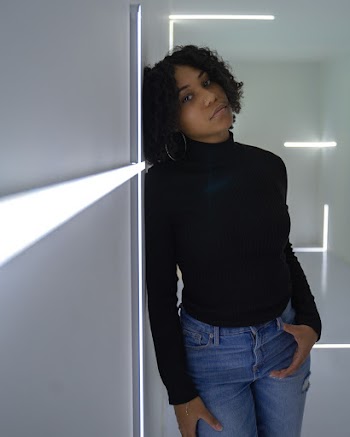 Photo of Woman in Black Pull Neck Sweater and Blue Jeans Leaning on Gray Wall Posing