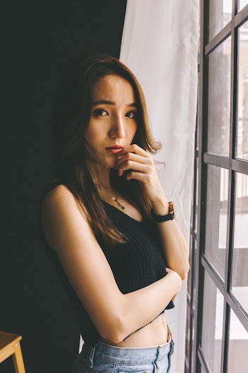 Photo of Woman in Black Sleeveless Crop Top and Blue Jeans Posing By Window