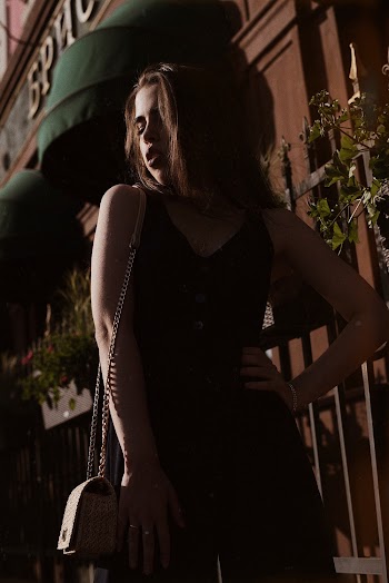 Photo of Woman in Black Sleeveless Jumpsuit and Crossbody Bag Posing Near Building