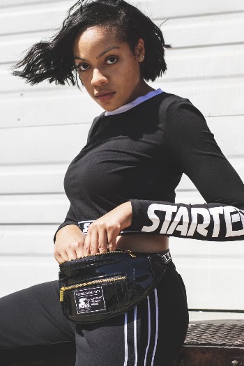 Photo of Woman in Black Starter Crop Top, Sweatpants and Fanny Pack Posing While Leaning on Metal Surface