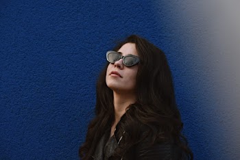 Photo of Woman in Black Sunglasses Posing By Blue Wall