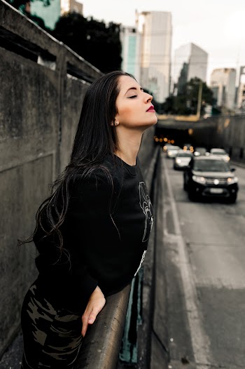 Photo of Woman in Black Sweater and Camouflage Pants  Leaning on Sidewalk Barrier With Her Eyes Closed