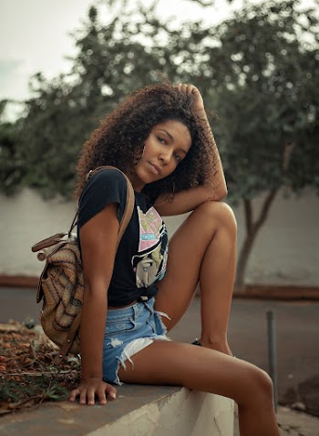 Photo of Woman In Black T-shirt and Blue Denim Shorts Posing While Sitting on Stone Railing