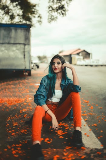 Photo of Woman in Blue Denim Jacket and Orange Pants Posing While Sitting on the Road