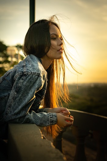 Photo of Woman in Blue Denim Jacket Leaning on Stone Railing