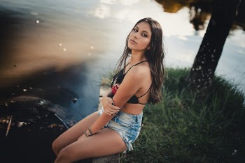 Photo of Woman in Blue Short Shorts and Black Crop Top Sitting on Stone Pavement by Body of Water