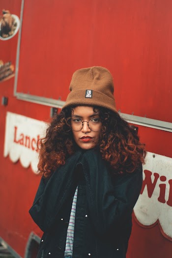 Photo of Woman in Brown Beanie Hat, Glasses, and, Black Jacket Standing In Front of Red Food Truck