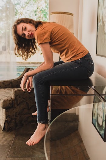 Photo of Woman in Brown T-shirt and Denim Jeans Sitting on Wooden Table