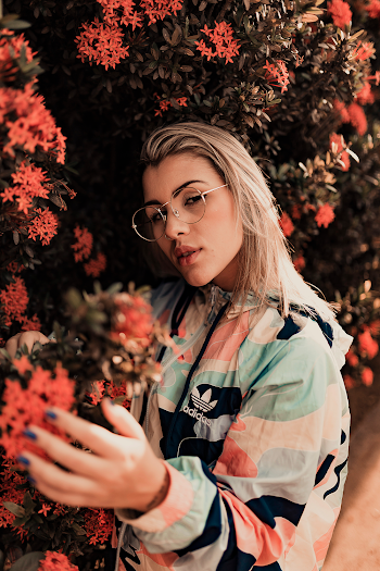 Photo of Woman in Camouflage Jacket Posing Next to Red Petaled Flower Bush