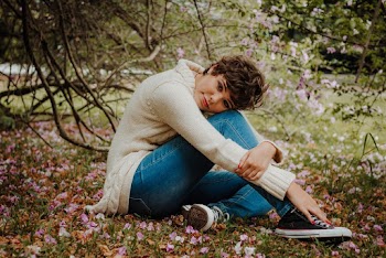 Photo of Woman in Cream Sweater and Blue Denim Jeans Sitting on the Ground