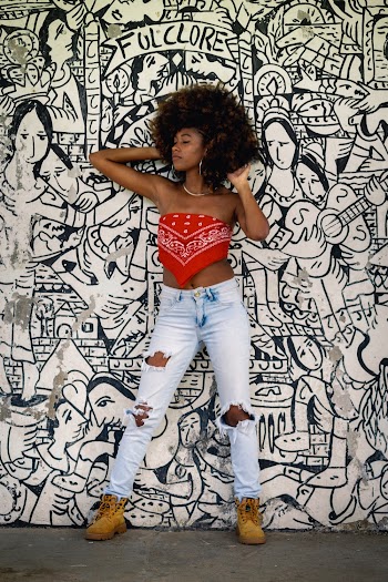 Photo of Woman in Distressed Blue Jeans Posing In Front of White Wall With Drawings 
