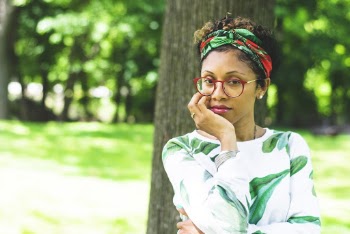 Photo of Woman in Eyeglasses and Headscarf Standing In Front of Tree Holding Her Chin