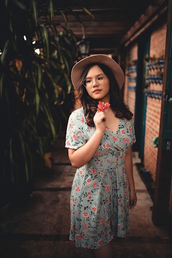 Photo of Woman in Floral Dress and Brown Hat Holding a Flower