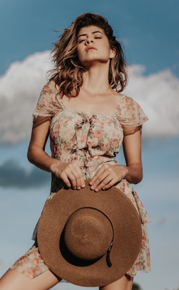 Photo of Woman in Floral Dress Holding a Sun Hat and Posing with Her Eyes Closed 
