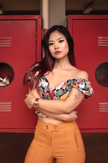 Photo of Woman in Floral Off-shoulder Crop Top and Orange Fitted Pants Posing with Her Arms Crossed