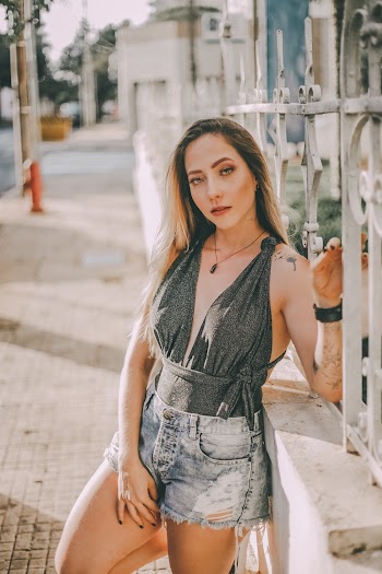Photo of Woman in Halter-strap Top and Blue Denim Shorts Leaning on White Fence