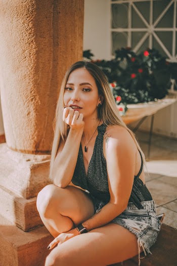 Photo of Woman in Halter-strap Top and Blue Denim Shorts Sitting Near Column