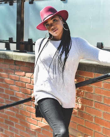 Photo of Woman in Maroon Fedora Hat, White Sweater, and Black Pants Leaning on Stair Railing