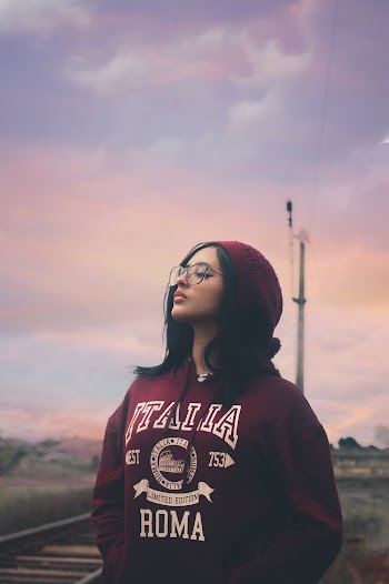 Photo of Woman in Maroon Hoodie and Beanie Hat Standing Next to Train Tracks