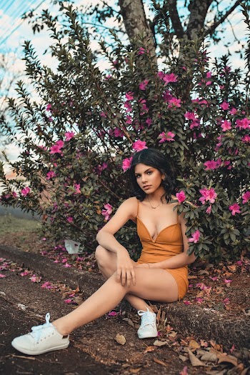Photo of Woman in Mustard Deep V-neck Spaghetti-strap Dress Sitting on the Curb by Pink Flower Plant