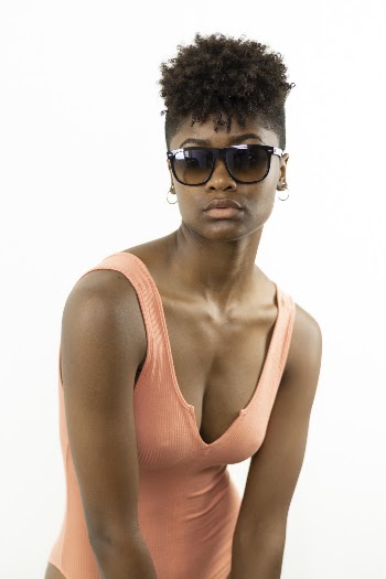 Photo of Woman in Orange Bodysuit and Sunglasses Posing In Front of White Background