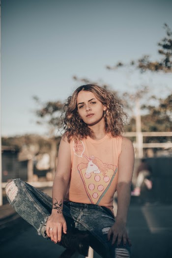 Photo of Woman in Orange Sleeveless Shirt and Blue Denim Jeans Sitting Outside