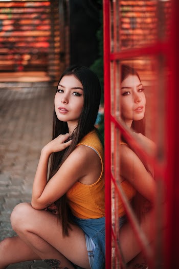 Photo of Woman in Orange Sleeveless Top Sitting on Floor Next to Glass Door