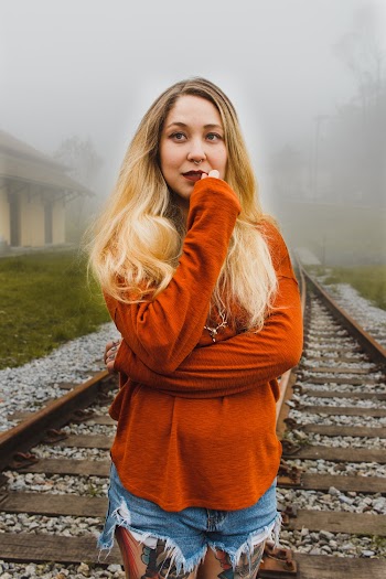 Photo of Woman in Orange Top and Blue Denim Shorts Standing on Train Tracks
