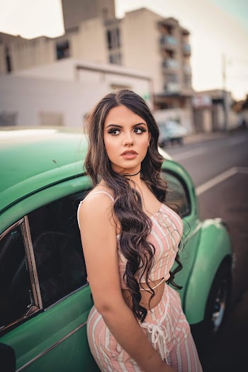 Photo of Woman in Pink and White Pinstriped Spaghetti Strap Top and Pants Leaning on Green VW Bettle Posing