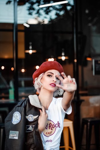 Photo of Woman in Red Beret, White T-shirt, and Brown Jacket Posing With Her Hand Out